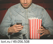 A young man with a bucket of popcorn is sitting in a cinema and is using his smartphone. Стоковое фото, агентство Ingram Publishing / Фотобанк Лори