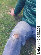 A trendy young man with a hole torn in his jeans at the knee is sitting on the grass. Стоковое фото, агентство Ingram Publishing / Фотобанк Лори