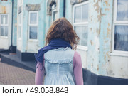 A young woman is standing in the street outside a blue house by the coast on a windy day. Стоковое фото, агентство Ingram Publishing / Фотобанк Лори