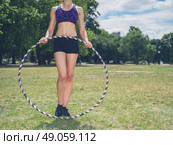 A fit young woman is standing on the grass in a park on a sunny summer day and is holding a hula hoop. Стоковое фото, агентство Ingram Publishing / Фотобанк Лори