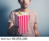 A young man is holding a box of popcorn with a cinema ticket in it. Стоковое фото, агентство Ingram Publishing / Фотобанк Лори