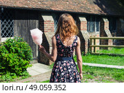 A young woman wearing a dress is standing outside an old farmhouse with a candyfloss on a sunny summer day. Стоковое фото, агентство Ingram Publishing / Фотобанк Лори