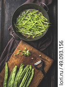 Green french beans cooking. Slices  Green french beans in cooking pot and vegetable peeler on dark rustic wooden background, top view. Стоковое фото, агентство Ingram Publishing / Фотобанк Лори