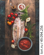 Fish cooking. Two pollack or coafish fillet on dark aged wooden background with tomato sauce, fresh tomatoes bunch, herbs and ingredients, top view. Стоковое фото, агентство Ingram Publishing / Фотобанк Лори