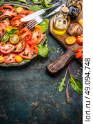 Tomatoes salad with various colorful tomatoes, olives oil and Balsamic vinegar . Plate with tomatoes salad, cutlery  and ingredients on dark rustic background, place for text, border, vertical. Стоковое фото, агентство Ingram Publishing / Фотобанк Лори