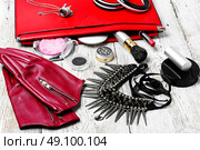 Red clutch bag and ladies accessories. Fashionable ladies handbag with cosmetics and decorations on light background. Стоковое фото, агентство Ingram Publishing / Фотобанк Лори