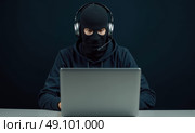 Мужчина в маске балаклаве и с гарнитурой за ноутбуком. Стоковое AI-изображение, AI-художник Илья Старков / Фотобанк Лори
