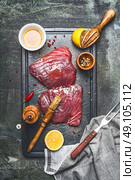 Raw tuna fish steak marinating with oil,lemon and rub brush on cutting board , top view, rustic background, dark styled. Стоковое фото, агентство Ingram Publishing / Фотобанк Лори