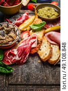 Italian smoked ham Prosciutto with crostini bread and specialties for antipasti on rustic wooden background, close up. Стоковое фото, агентство Ingram Publishing / Фотобанк Лори
