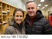 Warm Smiles in Winter Attire: middle-aged couple beams with joy, snugly dressed in their winter jackets, exuding warmth and companionship indoors. Стоковое AI-изображение, AI-художник Данила Большаков / Фотобанк Лори