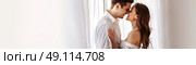 A man and woman share a romantic kiss in front of a window, showcasing their affection and intimacy. Стоковое AI-изображение, AI-художник Данила Большаков / Фотобанк Лори