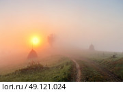 Sunrise over mountain field. Haystacks and road in misty rural hills. Foggy autumn morning in mountains. Стоковое фото, агентство Ingram Publishing / Фотобанк Лори