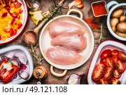 Raw chicken breasts , colorful cut vegetables in bowls , flavoring and cooking spoon. Preparation on rustic wooden background, top view. Стоковое фото, агентство Ingram Publishing / Фотобанк Лори