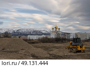 Строительные работы по благоустройству территории в северном городе. Вдали большой собор, городские здания и покрытые снегом сопки. На небе облака. Вид с Горохового поля на Свято-Троицкий собор. Город Магадан, Магаданская область, Дальний Восток России. Стоковое фото, фотограф Андрей Степанов / Фотобанк Лори