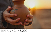 A child's small hands holding a clay water jug, symbolizing the thirst of Imam Hussain family, under the fading light of sunset. Стоковое AI-видео, аниматор Sergey Grishin / Фотобанк Лори