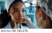 A dermatologist in a white coat and gloves examines a young woman’s facial acne scars under bright clinic lights. Стоковое AI-изображение, AI-художник Данила Большаков / Фотобанк Лори