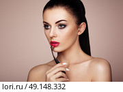 Beautiful woman paints lips with lipstick. Beautiful woman face. Makeup detail. Beauty girl with perfect skin. Red lips and nails manicure. Стоковое фото, агентство Ingram Publishing / Фотобанк Лори