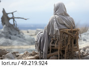 A cloaked person sits alone on a weathered wooden chair amidst a barren, rocky desert expanse, under a hazy sky. Стоковое AI-изображение, AI-художник Данила Большаков / Фотобанк Лори