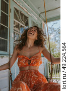 Cheerful woman joyfully laughing while sitting on a porch swing. Стоковое AI-изображение, AI-художник Данила Большаков / Фотобанк Лори