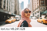 A beautiful hijabi woman wearing stylish sunglasses smiles at the camera while walking down an urban street in New York City. Стоковое AI-изображение, AI-художник Ярославский Максим / Фотобанк Лори