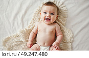 A small child is lying on a bed wrapped in an intricately tied blanket, top view. A child in the first moments of his life looks at the world and smiles. Стоковое AI-изображение, AI-художник Антон Слабоспицкий / Фотобанк Лори