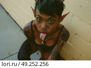 Elf-like woman with tattoos and piercings sticking out her tongue in a rebellious gesture. Стоковое AI-изображение, AI-художник Данила Большаков / Фотобанк Лори