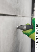 Close up of a gloved hand using an electric screwdriver with a riveter attachment to fix a slate wall with a metal exhaust construction rivet. Стоковое фото, фотограф Неведицына Елена / Фотобанк Лори