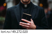 Priest holding a book in a formal setting while preparing for a religious ceremony during evening hours. Стоковое AI-изображение, AI-художник Сергей Толмачёв / Фотобанк Лори