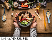 Vegetarian stir fry cooking preparation. Women female hands holding little wok pot with chopped vegetables for stir fry on kitchen table background with vegetables ingredients, top view. Стоковое фото, агентство Ingram Publishing / Фотобанк Лори