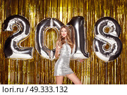 Beautiful Woman celebrating New Year. Girl with Glass of Champagne. Girl posing with Silver colored 2018 number Balloons over Golden sparkly background. Happy New Year. Стоковое фото, агентство Ingram Publishing / Фотобанк Лори