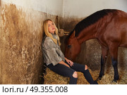 Blond woman on an indoor stable with horse. Blond woman on an indoor stable with a brown horse on straw bale. Стоковое фото, агентство Ingram Publishing / Фотобанк Лори