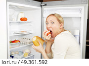 The woman greedy eats meal against an open refrigerator. Terrible hunger. Стоковое фото, агентство Ingram Publishing / Фотобанк Лори