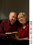 Elderly man and the woman reading the book on a dark background. Happy elderly spouses behind reading. Стоковое фото, агентство Ingram Publishing / Фотобанк Лори