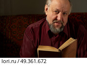 The Elderly man it is keen by reading of the book on a dark background. Wise man behind reading by the book. Стоковое фото, агентство Ingram Publishing / Фотобанк Лори