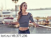 Blonde woman, model of fashion, standing in a harbor with boats and sea in the background. Beautiful young girl wearing striped t-shirt and blue jeans. Pretty russian female with pigtail. Стоковое фото, агентство Ingram Publishing / Фотобанк Лори