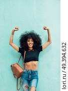 Funny black woman with afro hair raising arms outdoors. Female wearing casual clothes in urban background. Lifestyle concept. Стоковое фото, агентство Ingram Publishing / Фотобанк Лори