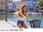 Girl riding a foldable e-bike in a Mediterranean marina port ebike. Стоковое фото, агентство Ingram Publishing / Фотобанк Лори