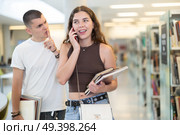 Male library patron makes remark to female student talking on phone. Стоковое фото, фотограф Яков Филимонов / Фотобанк Лори