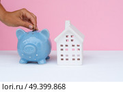 Someones hand putting coin into piggy bank with house beside, hypothec savings concept. Piggy bank, savings concept. Стоковое фото, агентство Ingram Publishing / Фотобанк Лори