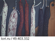 Cured meat and sausages hanging on black wooden background close up, retro toned. Cured meat and sausages. Стоковое фото, агентство Ingram Publishing / Фотобанк Лори