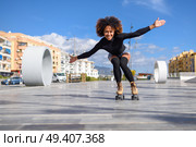 Young fit black woman on roller skates riding outdoors on urban street with open arms. Smiling girl with afro hairstyle rollerblading on sunny day. Стоковое фото, агентство Ingram Publishing / Фотобанк Лори