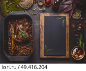 Slow cooked venison roast in black cast iron pan, top view. Braised leg of deer with bone and roasted vegetables in pot on dark rustic kitchen table background with copy space for design, top view. Стоковое фото, агентство Ingram Publishing / Фотобанк Лори
