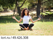 Young Arab woman doing yoga in nature. North African female wearing sport clothes doing lotus figure in urban park. Стоковое фото, агентство Ingram Publishing / Фотобанк Лори