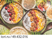 Smoothie mango bowls with chia seeds yogurt pudding and cranberries, nuts, oatmeal topping in coconut shells with spoon, top view. Healthy clean breakfast food. Стоковое фото, агентство Ingram Publishing / Фотобанк Лори
