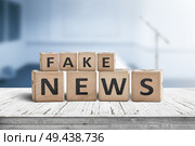 Fake news sign on a wooden desk in a blue room with a blurry background. Стоковое фото, агентство Ingram Publishing / Фотобанк Лори