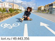 Young smiling black girl sitting on bike line and puts on skates. Woman with afro hairstyle rollerblading on sunny day. Young smiling black girl sitting on bike line and puts on skates. Стоковое фото, агентство Ingram Publishing / Фотобанк Лори