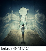 Abstract idea with a person standing in front of a big keyhole doorway surrounded by limitations daily routine concrete walls with clouds texture, casting a key shadow. Стоковое фото, агентство Ingram Publishing / Фотобанк Лори