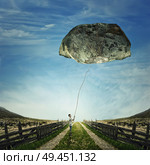 Surrealistic image as a young boy stand on a country road, holding a rope bound around a huge stone as a playing kite. Life pressure, stress and hard determination concept. Стоковое фото, агентство Ingram Publishing / Фотобанк Лори