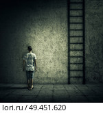 Abstract idea with a person standing in a dark room, in front of a concrete wall, figuring a ladder to escape. Surrounded by limitations, daily routine. Стоковое фото, агентство Ingram Publishing / Фотобанк Лори