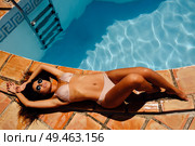 Relaxed woman sunbathing on the edge of a swimming pool with sunglasses, tanned perfect body, curly long hair, fashionable bright bikini. Relaxed woman sunbathing on the edge of a swimming pool . Стоковое фото, агентство Ingram Publishing / Фотобанк Лори